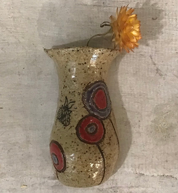 Decorative ceramic vase with red circular patterns and a small orange flower on a textured surface