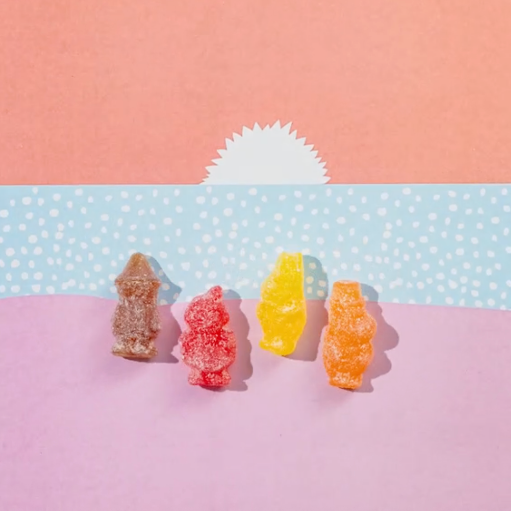 Four colorful gummy bears on a pink and blue polka dot background