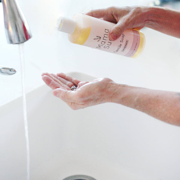 A person's hands pouring yellow liquid shampoo from a bottle labeled 'Yagana Sunrise' into their cupped hand, with running water from a chrome faucet in a white sink.