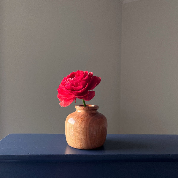 Wooden vase with a red flower on a dark surface against a plain background