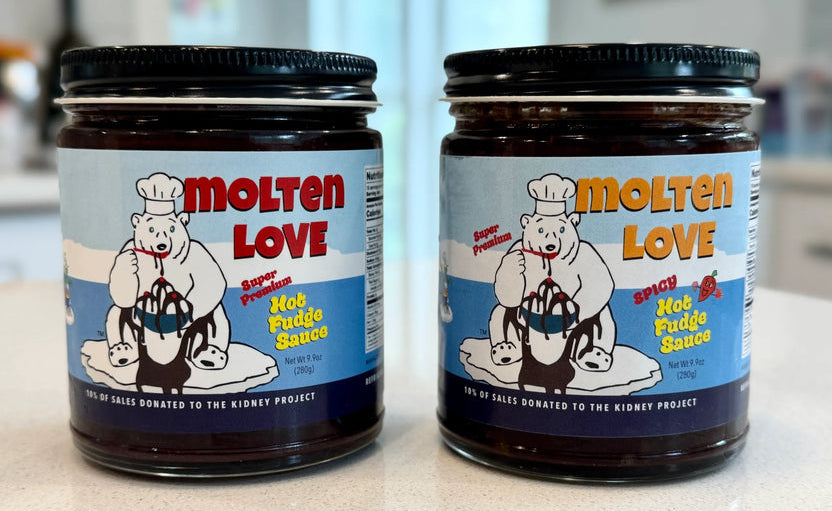 Two jars of Molten Love Spiced Hot Fudge Sauce on a light countertop, with a blurred kitchen background.