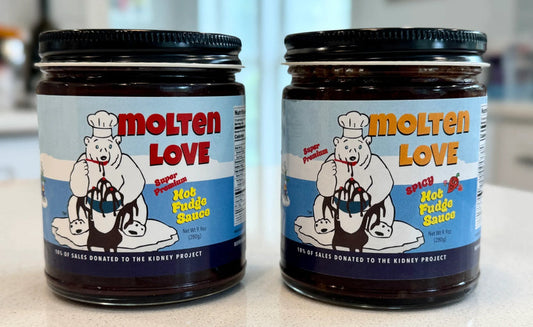Two jars of Molten Love Spiced Hot Fudge Sauce on a light countertop, with a blurred kitchen background.