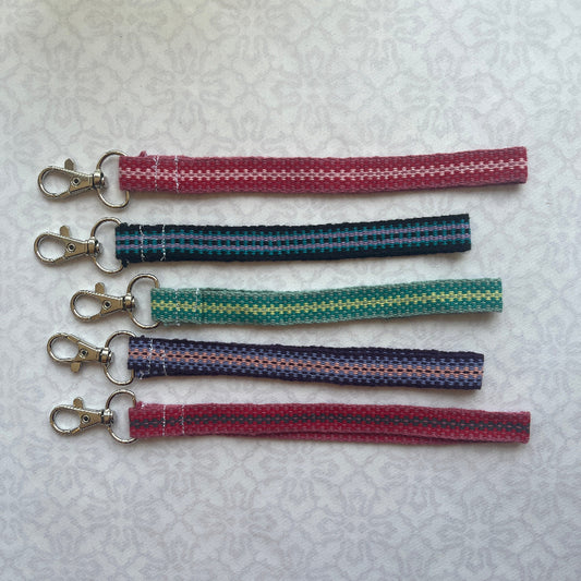 Five fabric keychains with metal clasps on a textured white background