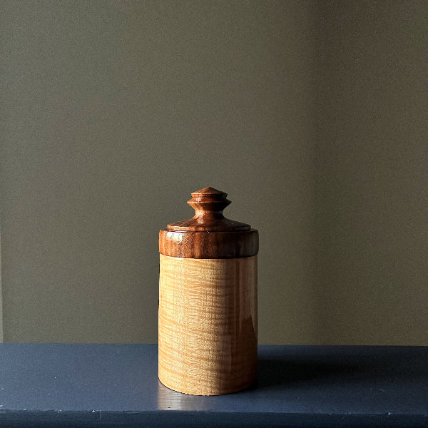 Wooden jar with a lid on a dark surface against a plain wall
