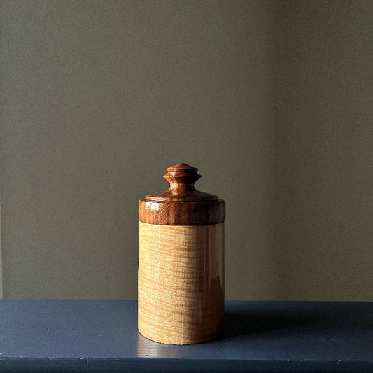 Wooden jar with a lid on a dark surface against a plain wall