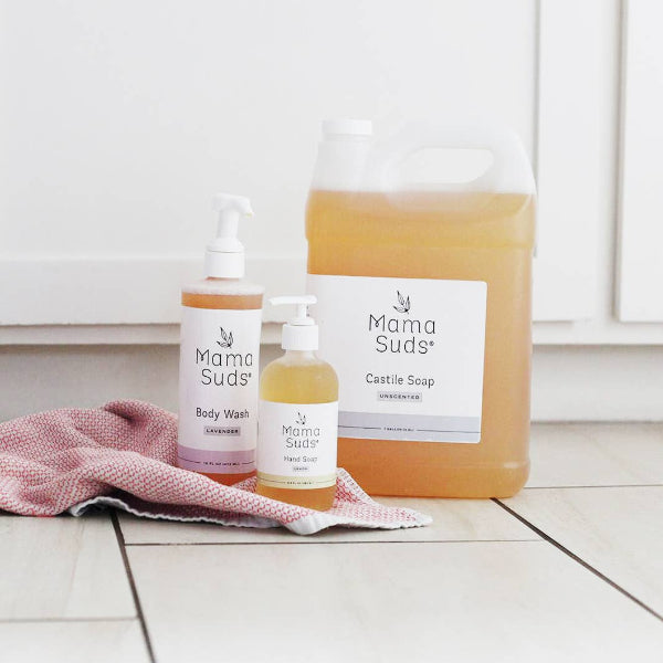 Mama Suds products including a bottle, a jar, and a towel on a white floor.