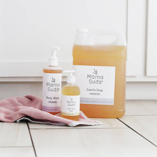 Mama Suds products including a bottle, a jar, and a towel on a white floor.