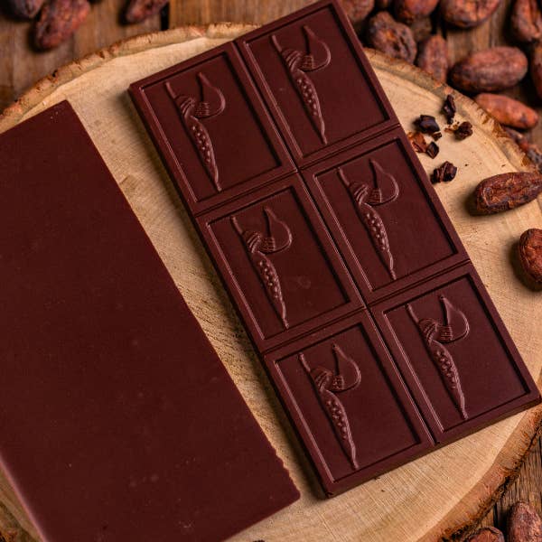 Dark chocolate bar with embossed designs on a wooden surface with cacao beans.
