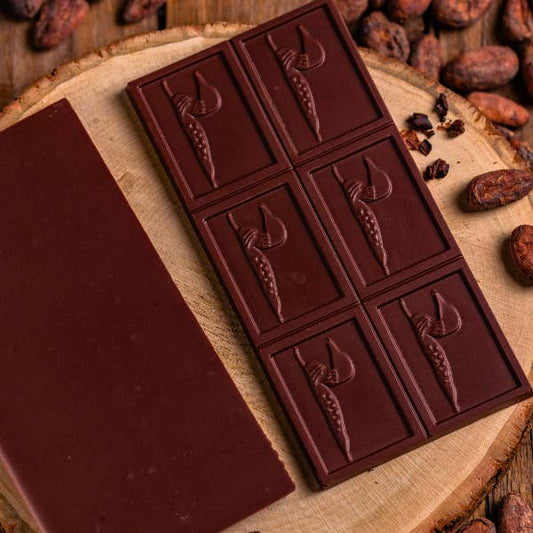 Dark chocolate bar with embossed designs on a wooden surface with cacao beans.