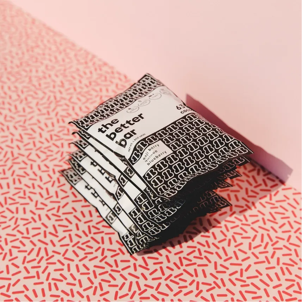 Stack of 'the better bar' packaging on a pink and red patterned surface
