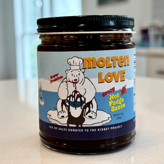 A jar of Molten Love Hot Fudge Sauce on a light countertop with a blurred kitchen background. The label features a cartoon polar bear wearing a chef's hat and holding a pot of red sauce, with the brand name 'Molten Love' in large orange letters.