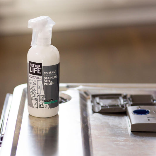 Spray bottle labeled 'Better Life' on a metallic surface with kitchen utensils in the background.
