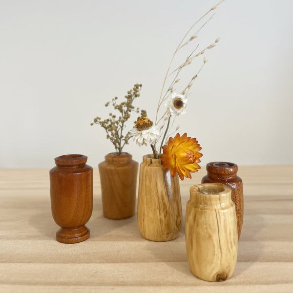 Set of wooden bud vases with dried flowers on a light wooden surface.