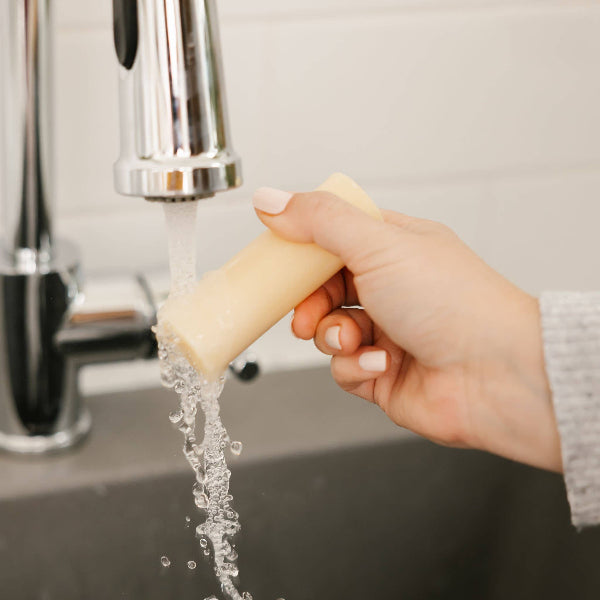Hand holding a bar of soap under running water from a faucet.